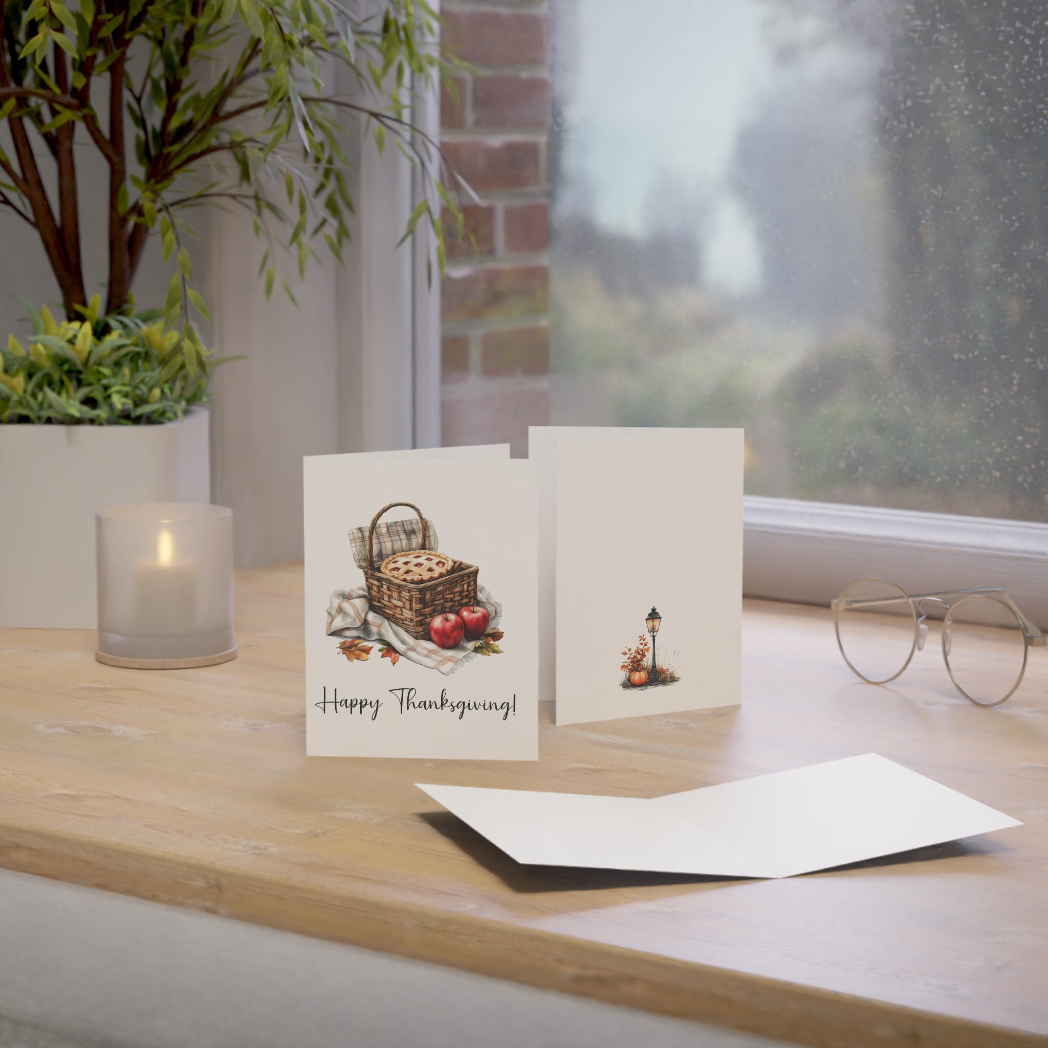 Two greeting cards on a wooden surface with a candle and plant in the background.
