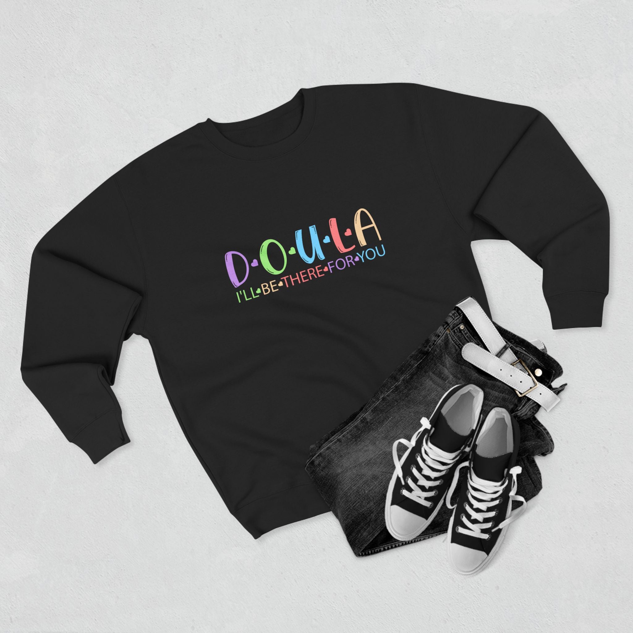 Black sweatshirt with colorful text DOULA I'll be there for you, black jeans, and black sneakers on a light gray background