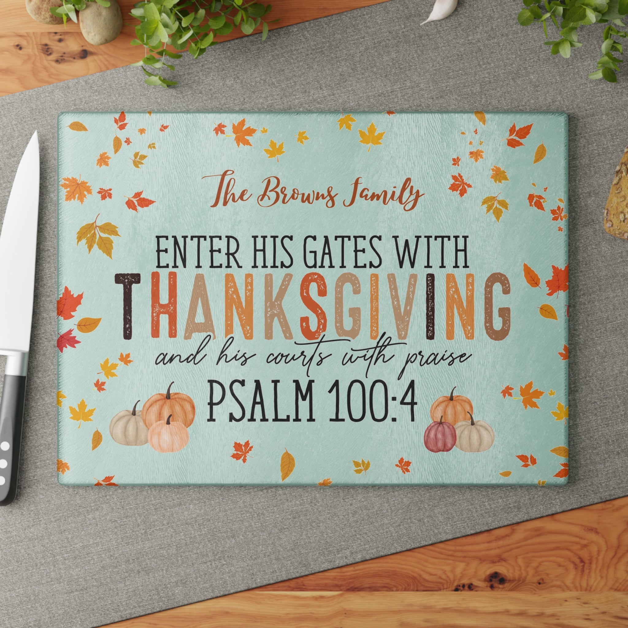 Decorative cutting board with Thanksgiving design and Psalm 100:4 text on a gray surface.