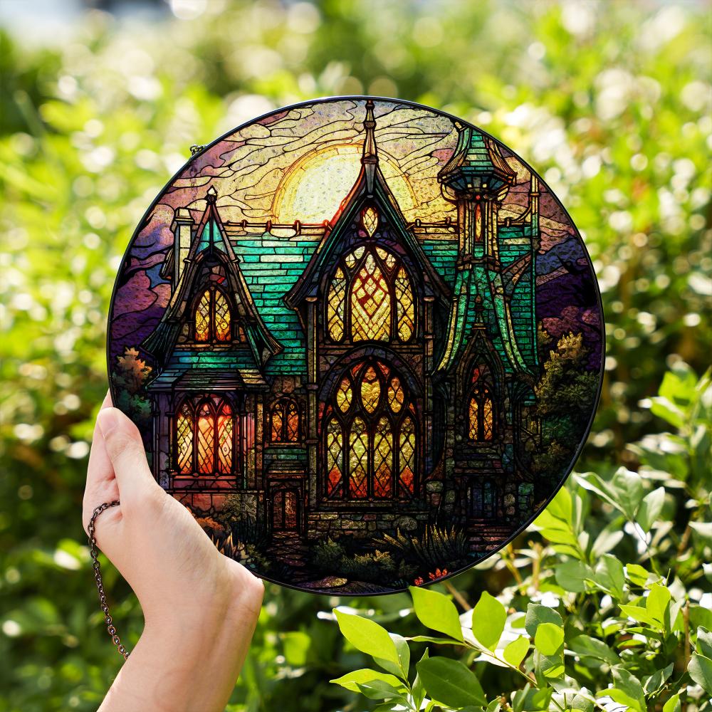 Stained glass suncatcher featuring a gothic mansion with a full moon, hanging in a window and glowing in natural sunlight.