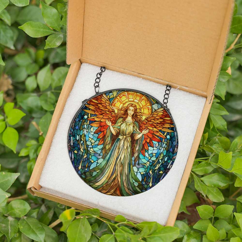 Stained glass angel suncatcher with vibrant red, blue, and gold tones, displayed in a gift box with black metal chain, set against a green leafy background