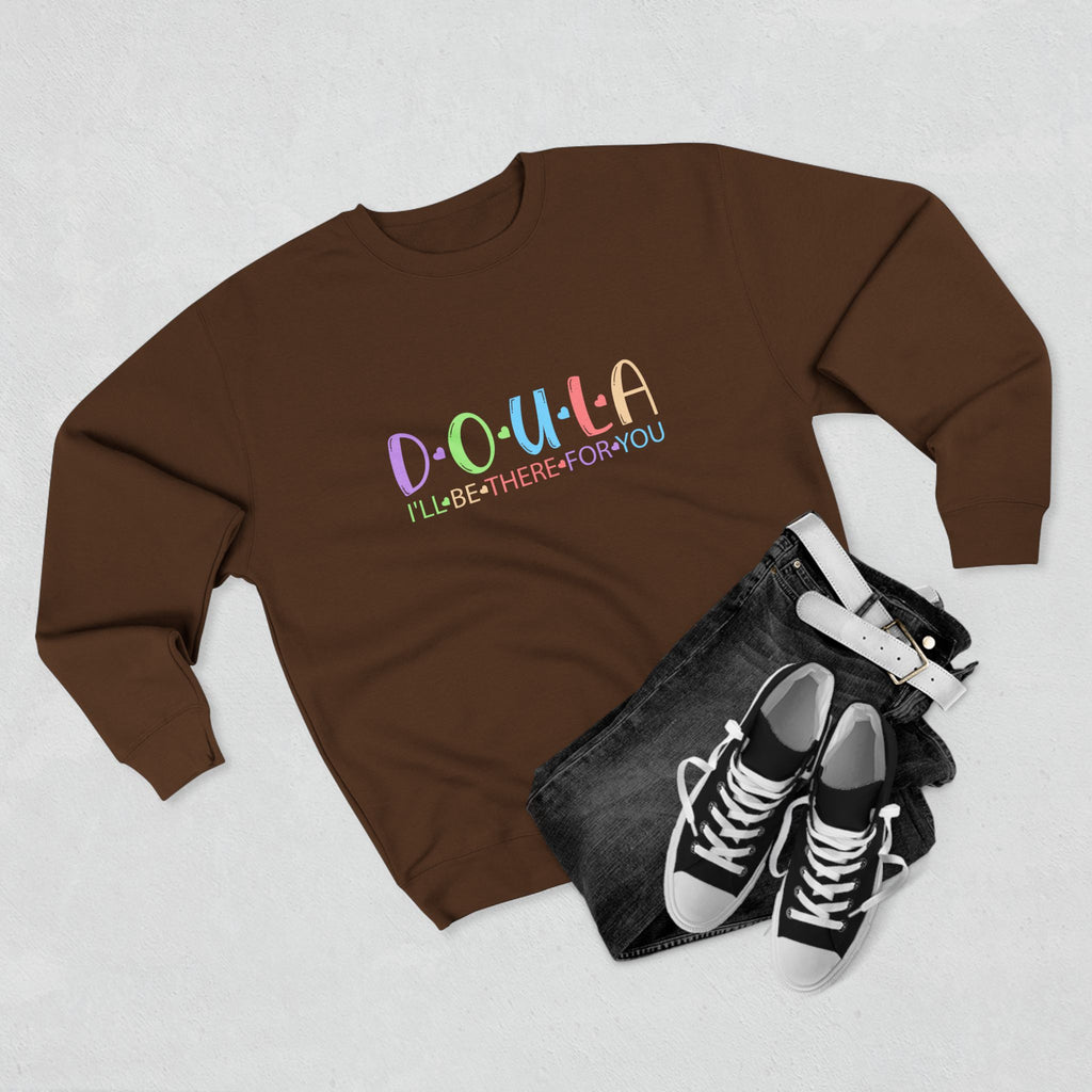 Brown sweatshirt with colorful text DOULA I'll be there for you, black denim jacket, and black sneakers on a light gray background