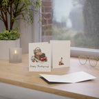 Two greeting cards on a wooden surface with a candle and plant in the background.
