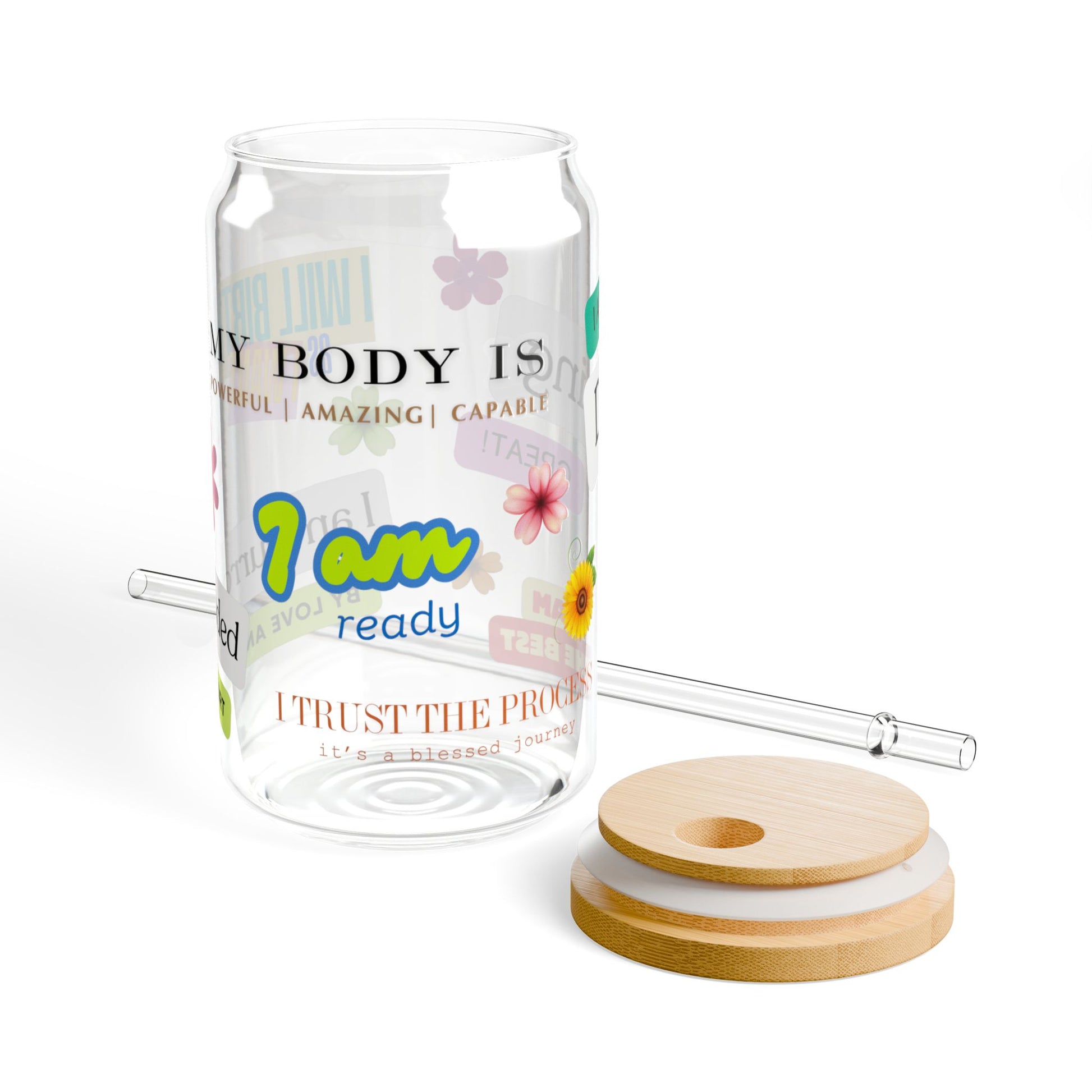 Glass tumbler with motivational text and floral design, accompanied by wooden coasters and a straw on a white background.