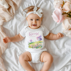 Baby onesie with "World is amazing" text and pastel nature design, made from soft 100% Airlume cotton, displayed flat with envelope neckline and snap closures.