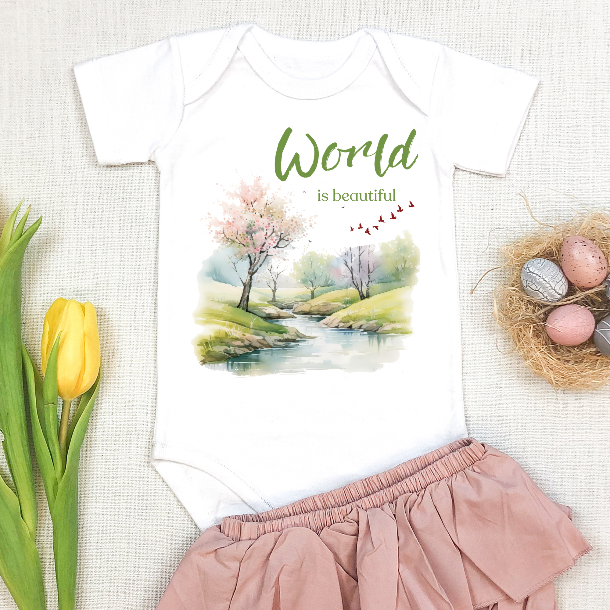Baby onesie with "World is beautiful" text and pastel nature design, made from soft 100% Airlume cotton, displayed flat with envelope neckline and snap closures.