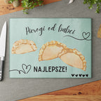 Glass cutting board with pierogi design and text on a white brick wall background