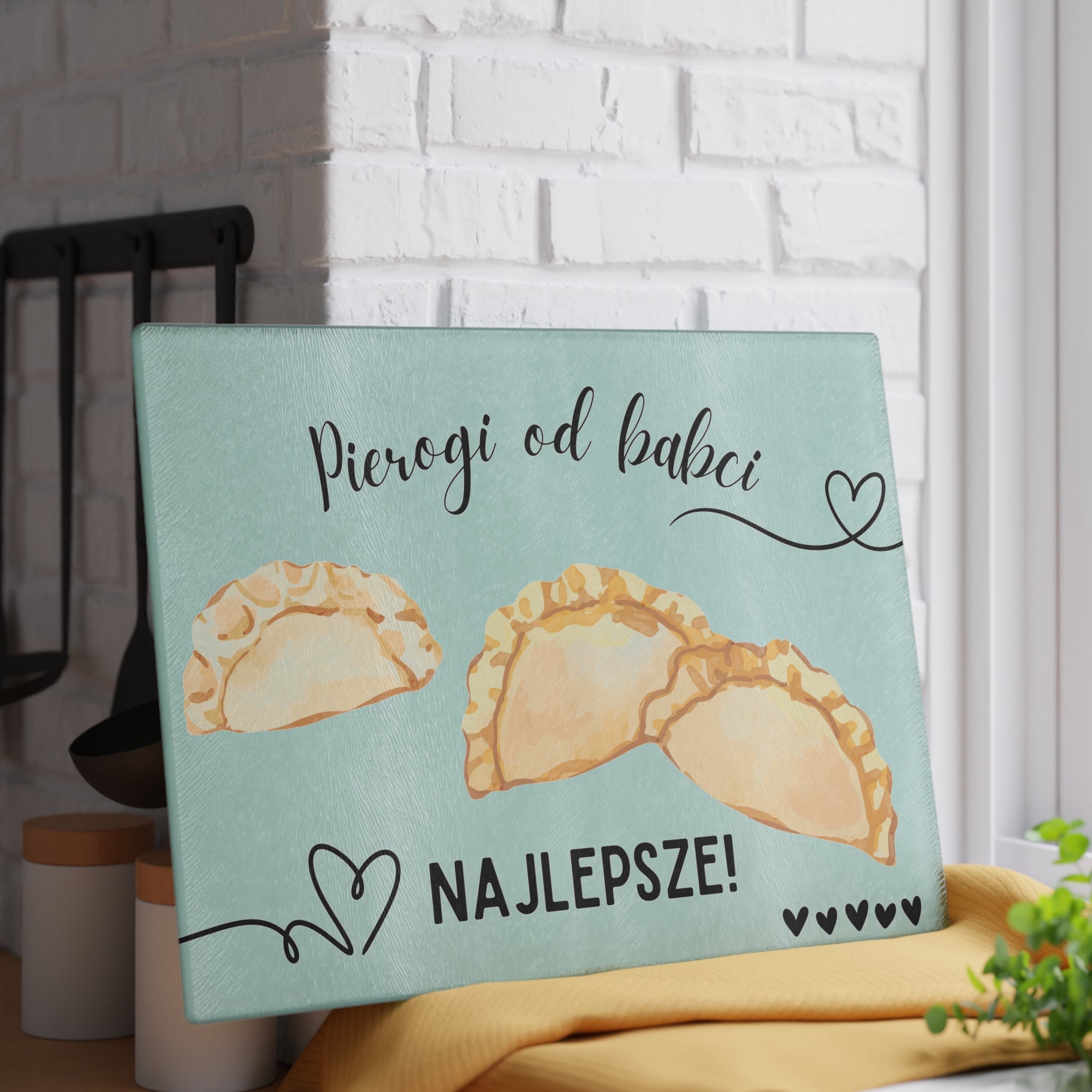 Glass cutting board with pierogi design and text on a white brick wall background