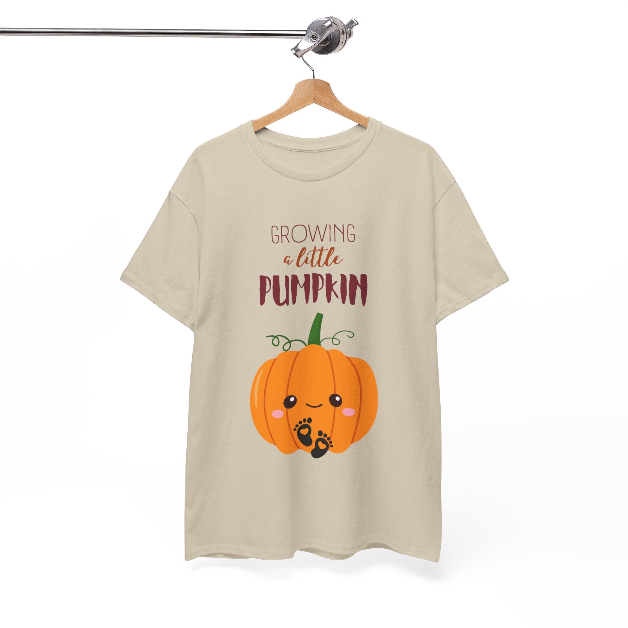 Beige t-shirt with a pumpkin graphic and text on a hanger against a white background
