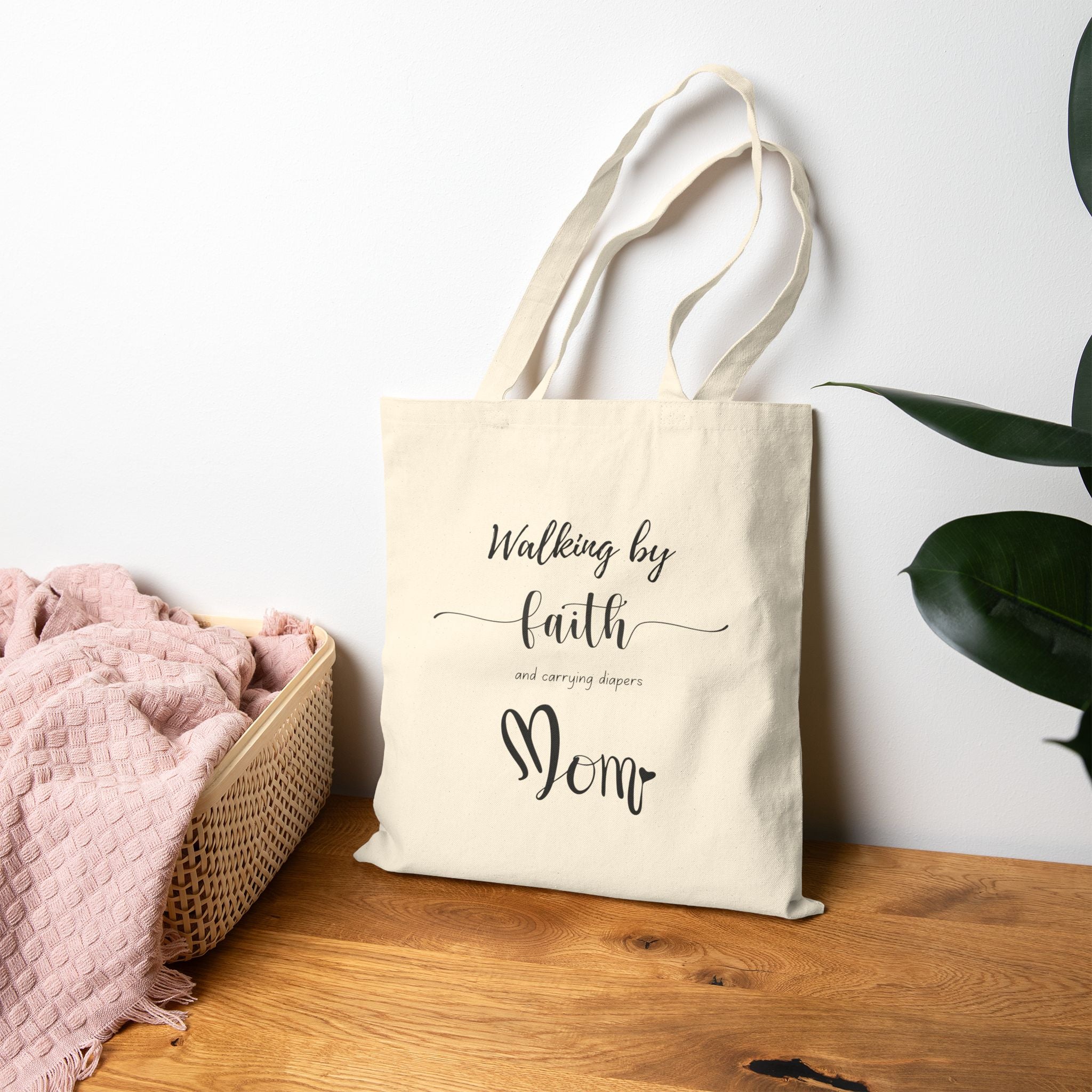 Natural cotton Christian tote bag with 'Walking by Faith and Carrying Diapers' text, designed for moms, featuring sturdy canvas handles and faith-inspired message.
