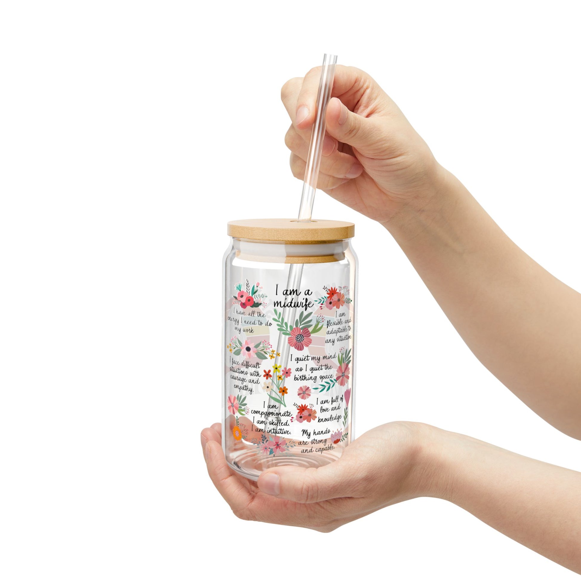 Hand holding a glass tumbler with a wooden lid and floral design on a white background