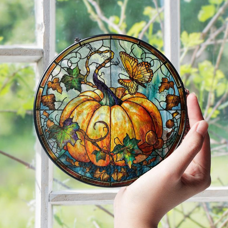 Stained glass pumpkin with leaves and butterflies held in front of a window with greenery outside.