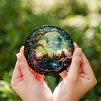Person holding a round, intricately designed stained glass suncatcher against a blurred green background