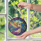 Colorful stained glass suncatcher with angel design held by a hand against a window with greenery