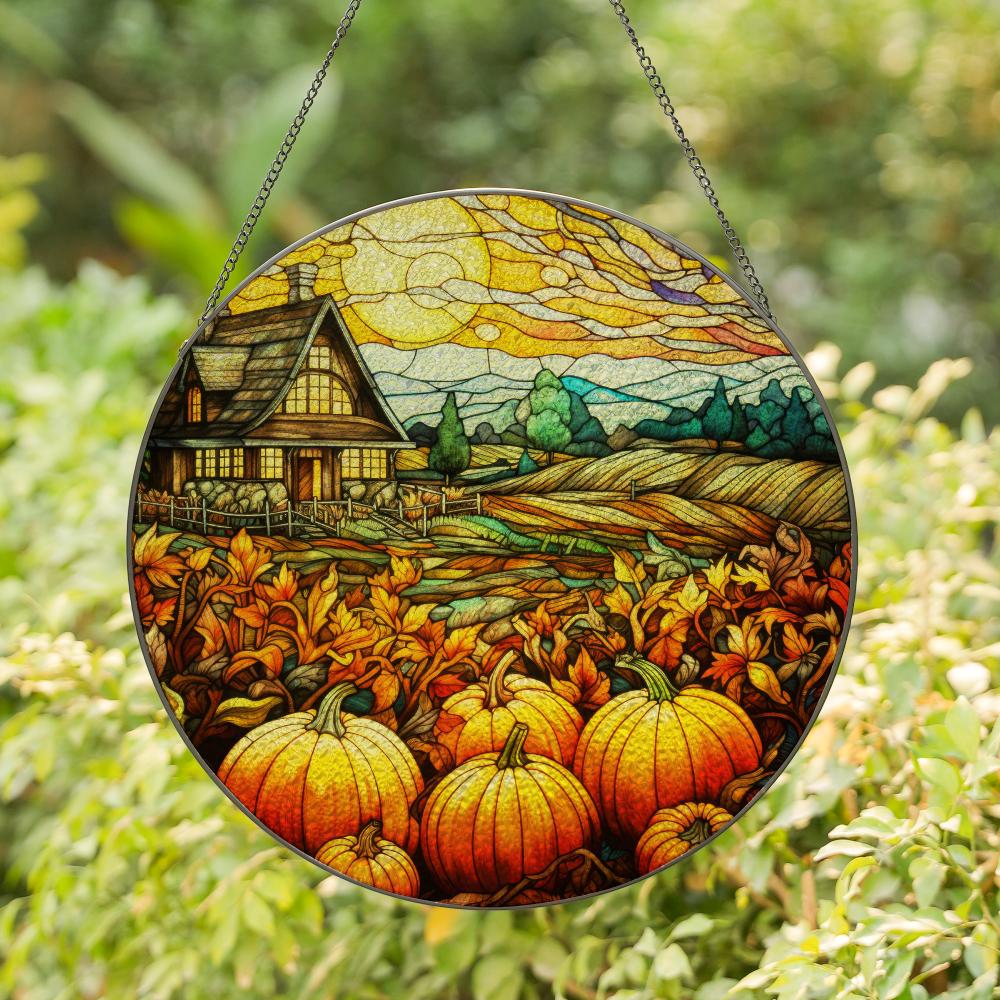 Round stained glass panel with autumn scene featuring pumpkins and a house, hanging outdoors.