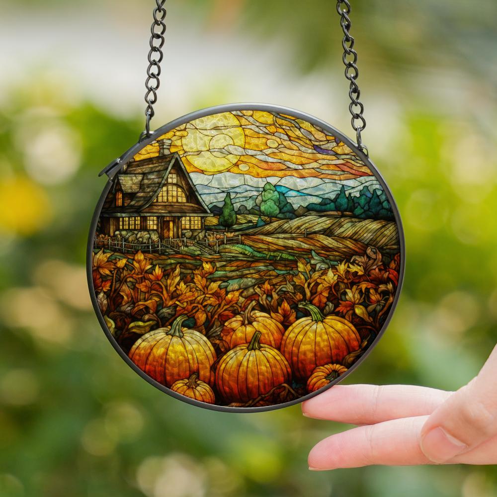 Round stained glass panel with autumn scene held by a hand against a blurred green background